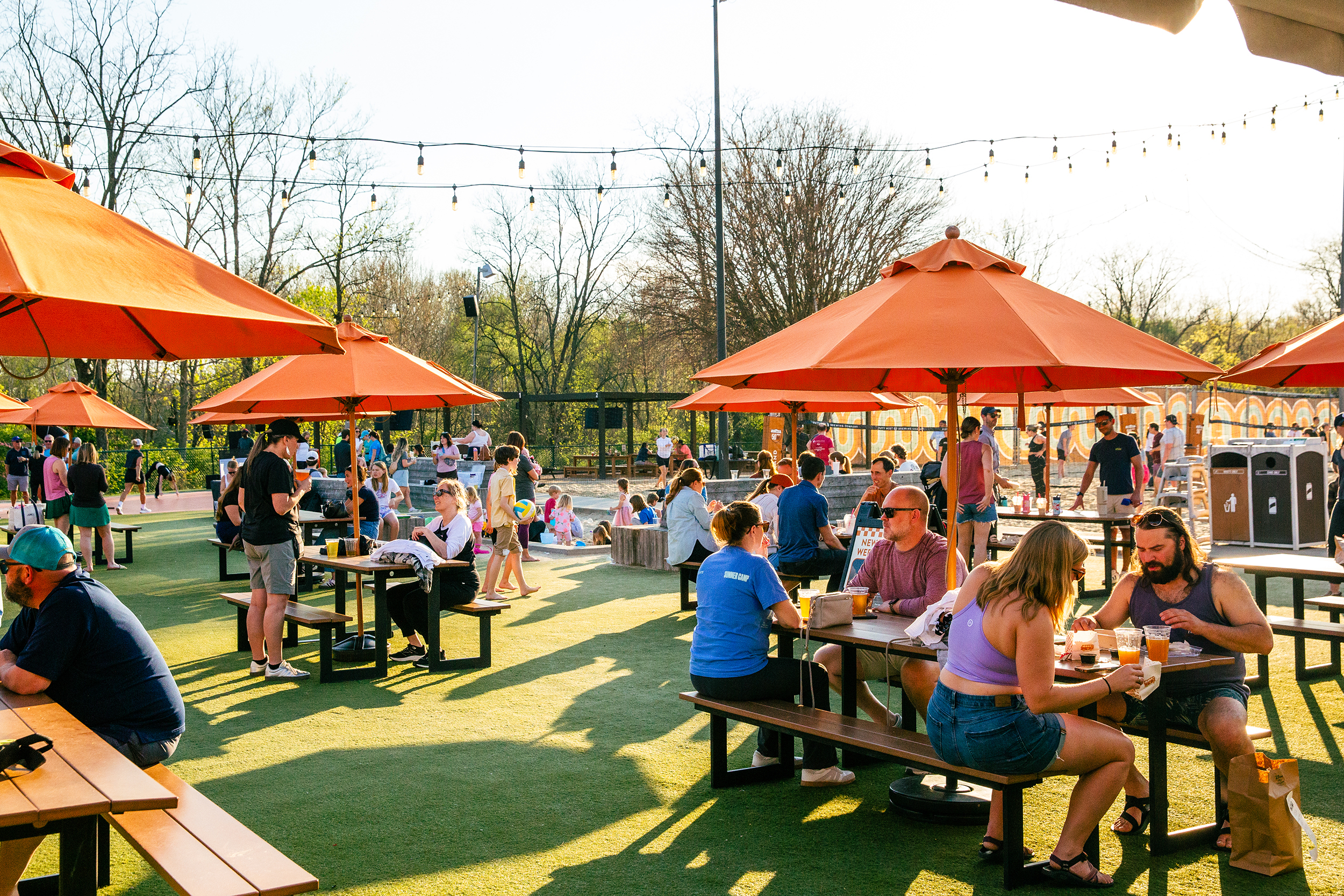 Families and friends spread across picnic tables under orange umbrellas on the Fifty West lawn